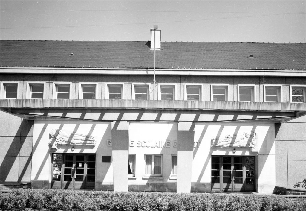 Photographie noir et blanc de la façade de l'école Carnot avec les deux bas-reliefs de Roger Prat.