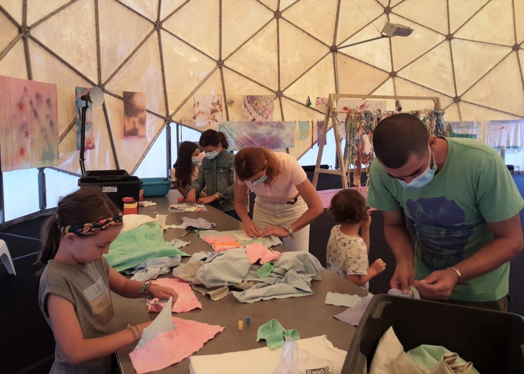 Enfants et adultes découpant des bandes de tissu teinté lors d'un atelier dans le Radôme.