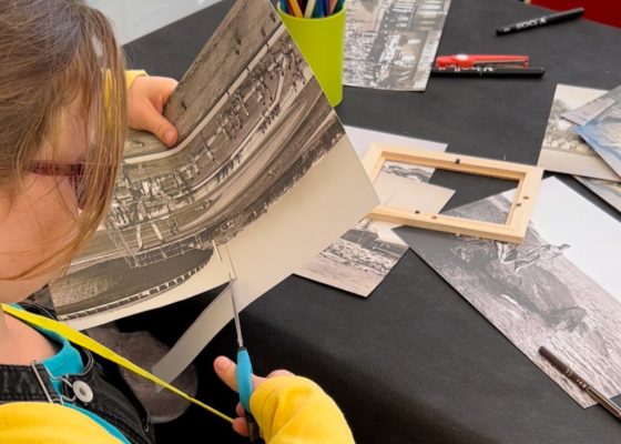 Une enfant de dos découpe une photographie pour créer sa carte postale lors d'un atelier à l'Écomusée.