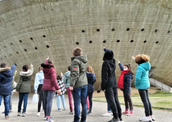 Groupe d'élèves vu de dos pointant du doigt la Soucoupe lors d'une activité pédagogique.