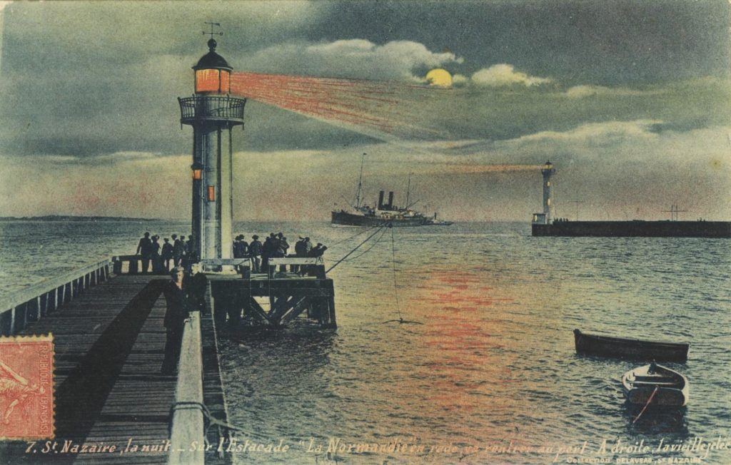 Carte postale illustrée représentant l'une des estacades de l'entrée est et le vieux môle de nuit, au loin un paquebot s'avance alors que le feu de l'estacade projette une lumière orangée sur la mer.