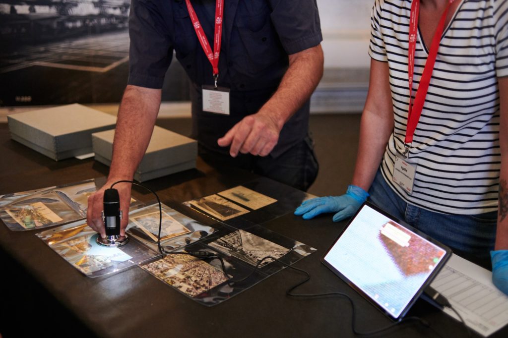 Gros plan sur les mains d'un médiateur de l'Écomusée alors qu'il passe un microscope numérique sur une carte postale lors d'une visite flash.