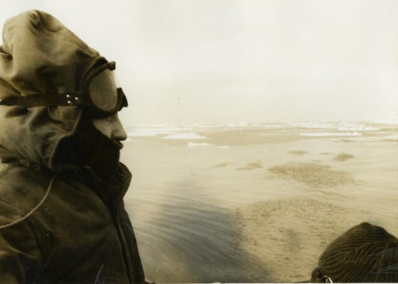 Photographie noir et blanc des années 1960, représentant un sous-marinier chaudement vêtu regardant la banquise depuis le kiosque d"un sous-marin.