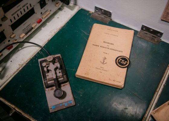 Photographie en gros plan du bureau du poste radio du sous-marin Espadon avec le manipulateur Morse et le manuel du marin radiotélégraphiste.