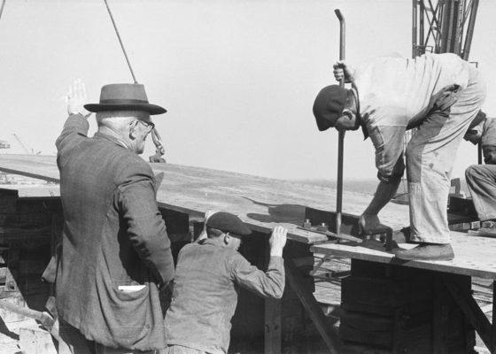 Photographie noir et blanc de deux charpentiers fer et un sous-chef d'atelier lors de la mise en place des deux premières tôles du paquebot France (1962), le 7 octobre 1957.