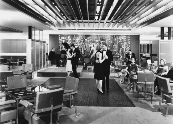 Photographe : inconnu. Collection Saint-Nazaire Agglomération Tourisme - Écomusée. Fonds Chantiers de l’Atlantique. Photographie en noir et blanc représentant deux couples de danseurs valsant dans le fumoir deuxième classe du paquebot France.