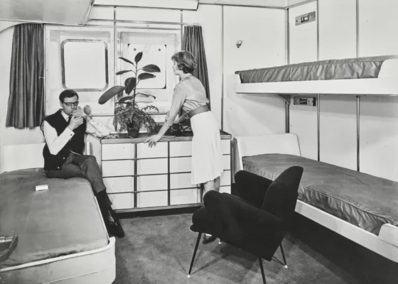 Photographe : inconnu. Collection Saint-Nazaire Agglomération Tourisme - Écomusée. Fonds Chantiers de l’Atlantique. Photographie noir et blanc d'un couple de passagers dans une cabine de classe touriste à quatre lits du paquebot France (1962).