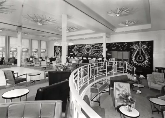 Photographe : inconnu. © ADAGP, Paris 2024. Décorateur : André Arbus. Collection Saint-Nazaire Agglomération Tourisme - Écomusée. Fonds Chantiers de l’Atlantique. Photographie noir et blanc du fumoir 1re classe du paquebot France (1962), conçu par le décorateur André Arbus avec des canapés, des fauteuils, des tables basses et le mur du fond recouvert par la tapisserie Soleil d'Orphée de Picart-Ledoux.