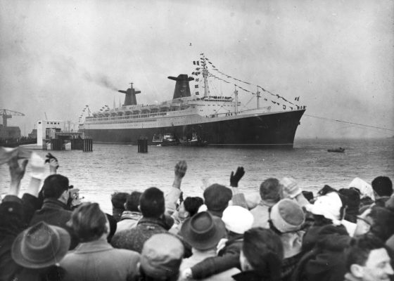 Photographie noir et blanc du paquebot France sortant du port de Saint-Nazaire, au premier plan une foule agite les bras.