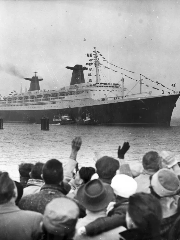 Photographie noir et blanc du paquebot France sortant du port de Saint-Nazaire, au premier plan une foule agite les bras.