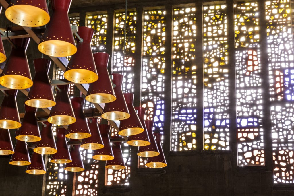 Photographie des vitraux de Serge Rezvani, vus de l'intérieur de l'église Sainte-Anne, avec au premier plan des luminaires suspendus.