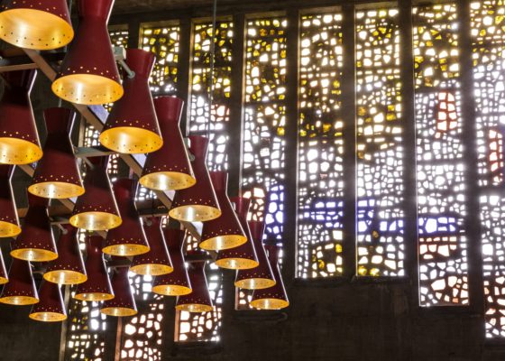 Photographie des vitraux de Serge Rezvani, vus de l'intérieur de l'église Sainte-Anne, avec au premier plan des luminaires suspendus.