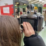 Photographie d'une collégienne en plein reportage photographique avec un appareil argentique dans les halles de Saint-Nazaire.