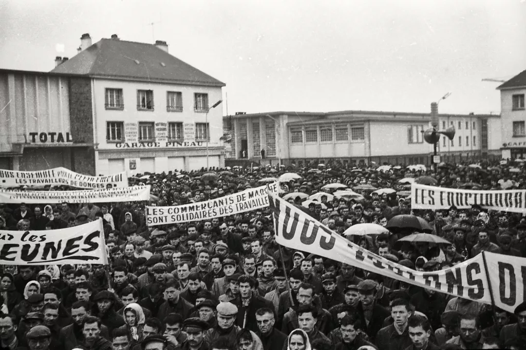 Sur une place du marché noire de monde, fonctionnaires, commerçants, travailleurs de la métallurgie, des raffineries et d’autres secteurs affichent leur solidarité avec les ouvriers licenciés de 1964.