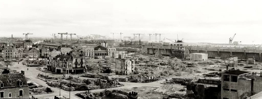 Photographie panoramique représentant l'ancien centre-ville de Saint-Nazaire en ruines lors de son déblaiement, avec la base sous-marine en arrière-plan.