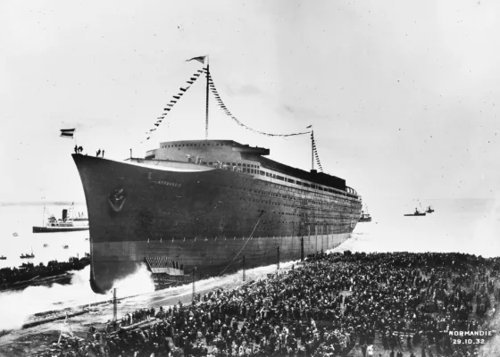 Photographie en noir et blanc du lancement du paquebot Normandie le 29 octobre 1932 à Saint-Nazaire, glissant vers l'eau devant une foule immense rassemblée sur les quais.